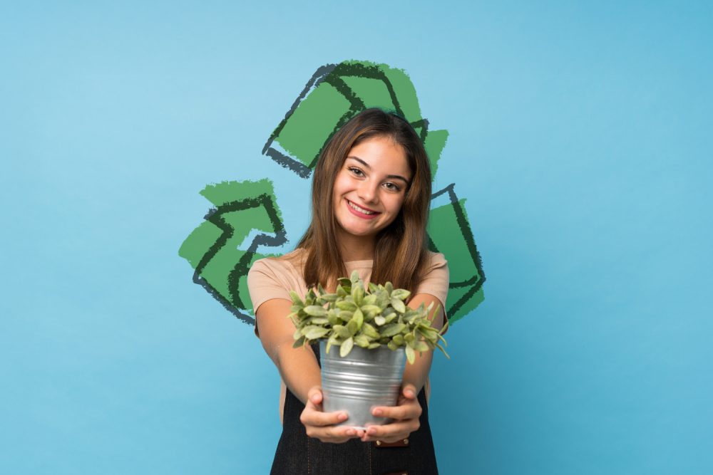 Eco event w M1 Czeladź. Dziewczyna trzymająca w rękach roślinkę, trzmielinę. Piktogram przedstawiający znak ekologii na drugim planie.