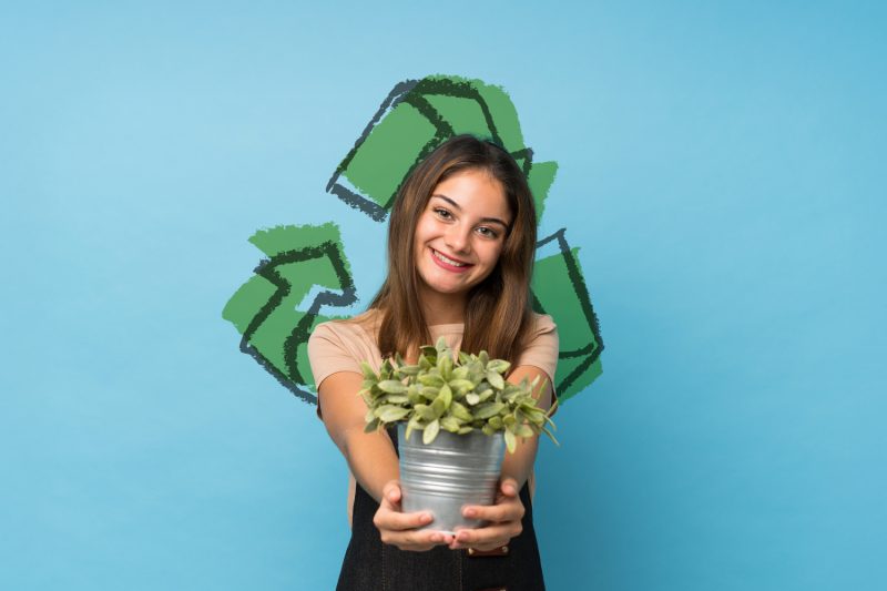 Eco event w M1 Czeladź. Dziewczyna trzymająca w rękach roślinkę, trzmielinę. Piktogram przedstawiający znak ekologii na drugim planie.