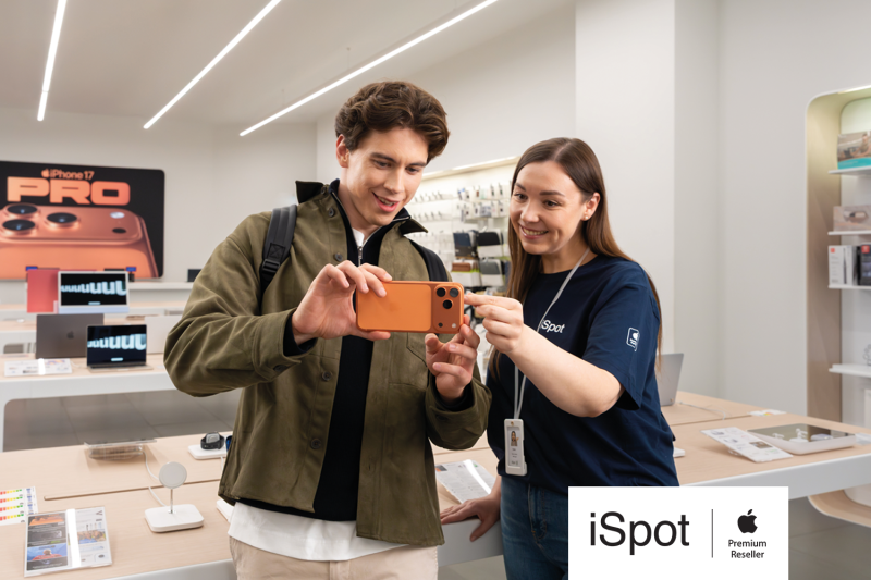 Grafika promująca otwarcie iSpot w M1 Czeladź. Ekspedientka sklepu przedstawiająca sprzęt Apple klientowi.